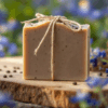 alt="Coffee cedar soap with fine coffee grounds, tied with natural twine, displayed on wooden surface with Texas bluebonnets and coffee beans"